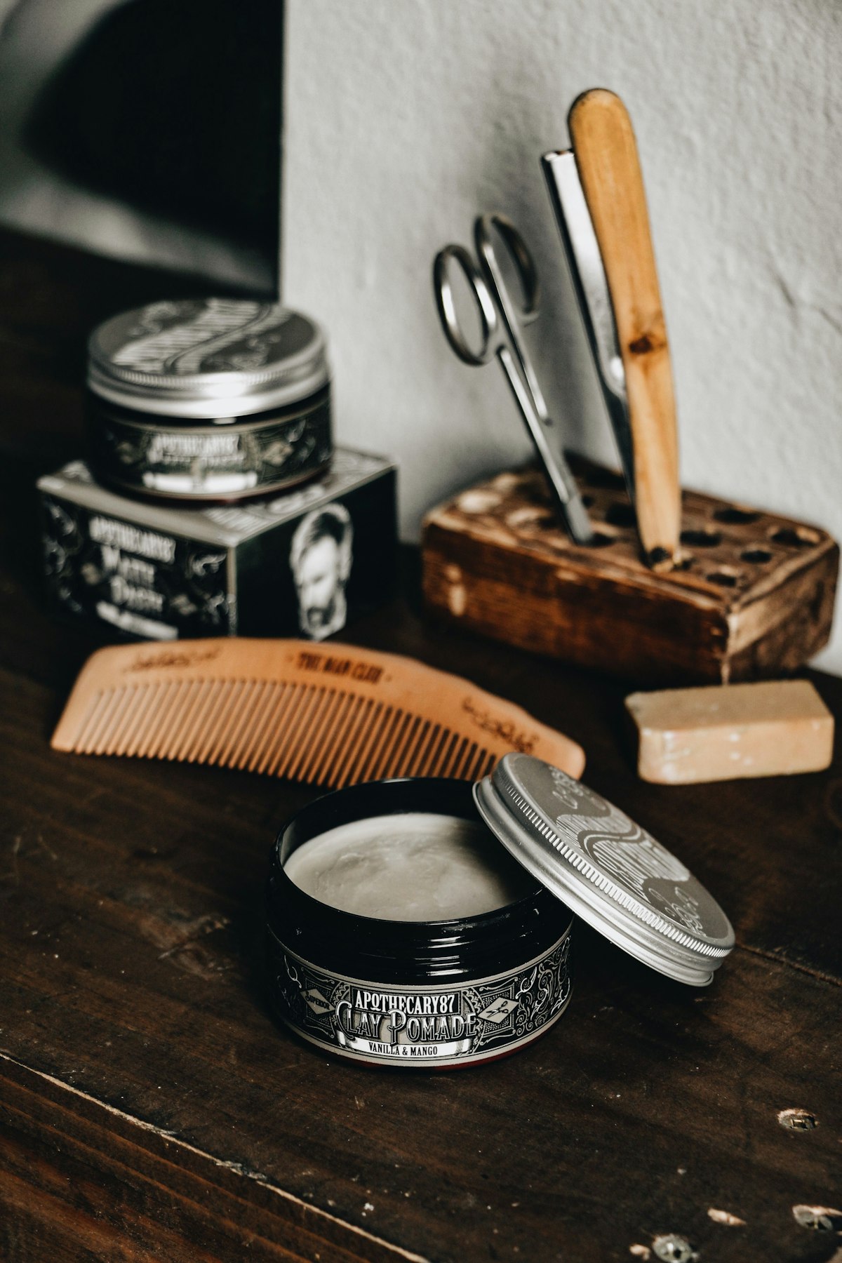 Barber grooming tools — comb, scissors, razor, and pomade on a wooden counter